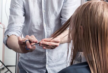 A hairdresser making haircut for a blonde female client in hairdressing salon. Selective focusの写真素材