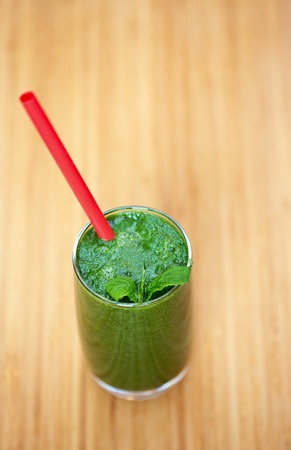A glass of green smoothie with tube on wooden backgroundの写真素材