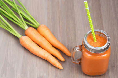 Healthy carrot smoothie in a jar with tube wooden background. Shallow dofの写真素材