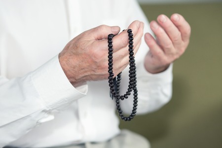 Praying hands of an old man holding rosary beads. Selective focus
