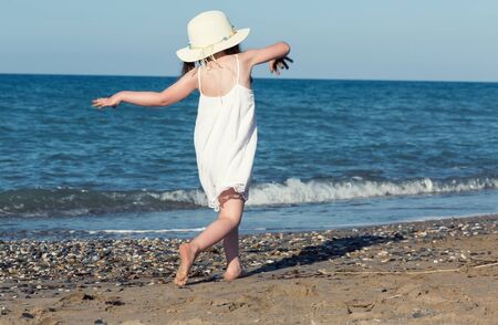 Little girl in white dress walking alone the sea, playing on the seashoreの写真素材