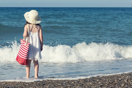 Little girl in white dress walking alone the sea, playing on the seashoreの写真素材