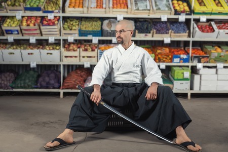 A man against the background with racks with fruits and vegetables dressed in Japanese kimono and hakama holding katana.の写真素材