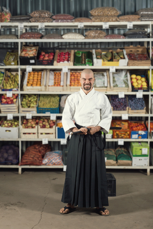 A man against the background with racks with fruits and vegetables dressed in Japanese kimono and hakama holding katana.の写真素材