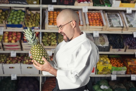 AVery hungry man against the background with racks with fruits and vegetables dressed in Japanese kimono and hakama holding a pineappleの写真素材