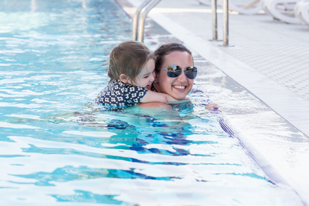 Happy mother and her daughter playing in swimming poolの写真素材