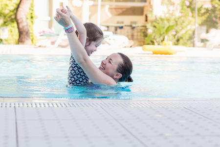 Happy mother and her daughter playing in swimming poolの写真素材
