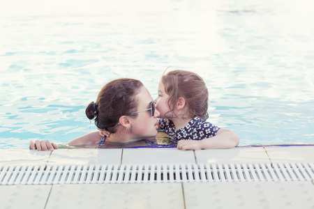 Happy mother and her daughter playing in swimming poolの写真素材