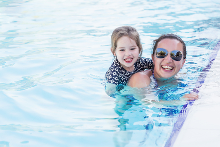 Happy mother and her daughter playing in swimming poolの写真素材