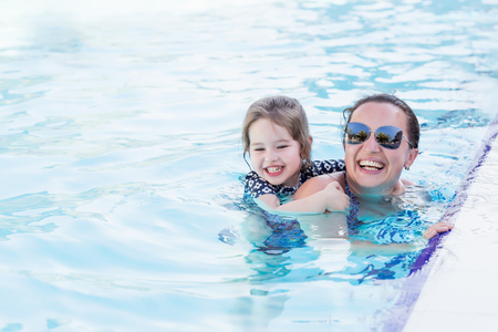Happy mother and her daughter playing in swimming poolの写真素材