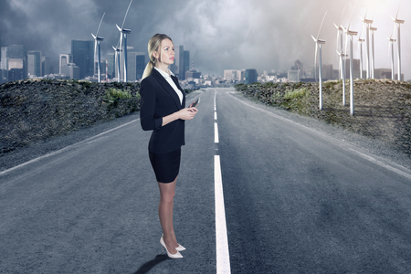 Businesswoman standing on road and a windfarmの写真素材