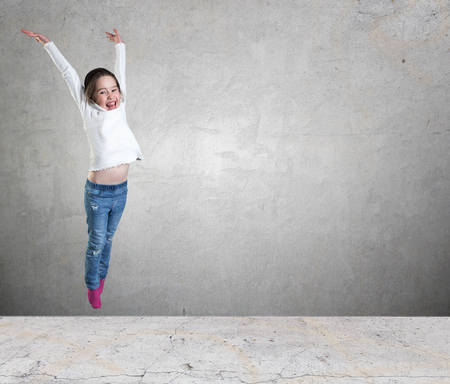 Happy little girl jumping in the air against a concrete wall backgroundの写真素材