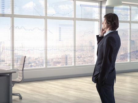 Businessman talking on phone while anaylzing financial charts on virtual displayの写真素材