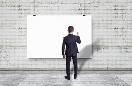 Businessman drawing on white backdrop against white brick wallの写真素材