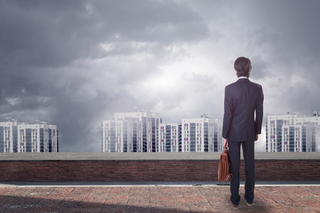Back view of young businessman on rooftop looking at city with copy space.の写真素材