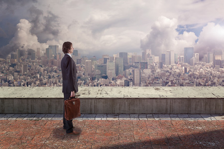 Side back view of a businessman on rooftop looking at city with copy space.の写真素材