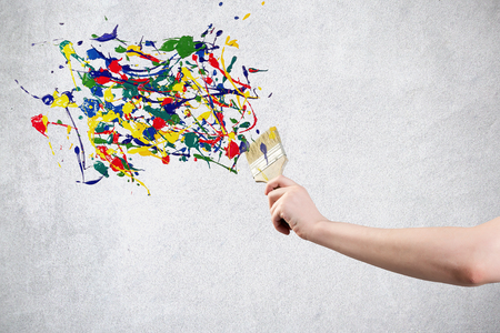 A hand holding paintbrush creating colorful paint splashesの写真素材