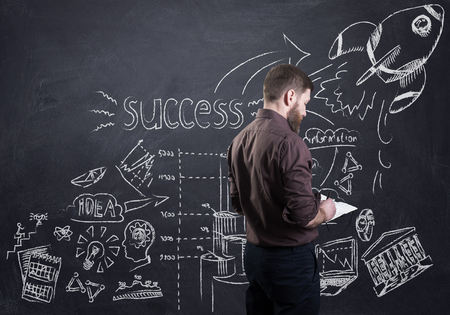 A bearded businessman presenting his business plan drawn on black boardの写真素材