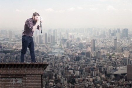 Handsome bearded man on a roof top taking picture of a cityの写真素材