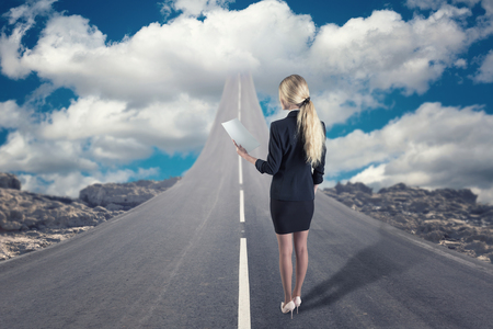 A businesswoman standing on road that goes up to the skyの写真素材