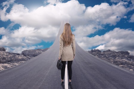 A businesswoman standing on road that goes up to the skyの写真素材