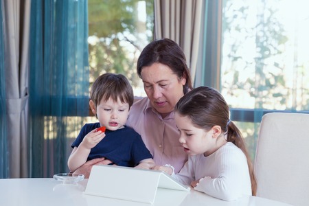 Grandma entertaining her little grandchildren with a tablet computer gameの写真素材