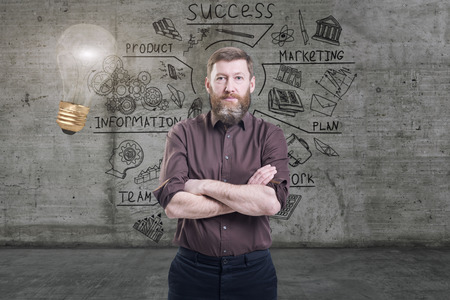 Handsome businessman against a concrete wall with sketch drawn on it and bright lightbulbの写真素材