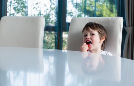 Cute boy eating fresh ripe strawberries at homeの写真素材