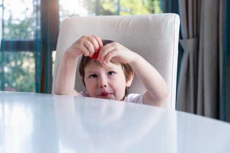 Cute boy eating fresh ripe strawberries at homeの写真素材