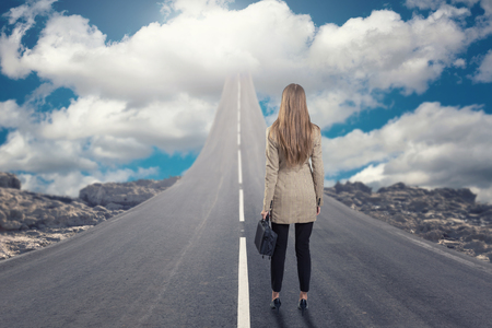 A businesswoman standing on road that goes up to the skyの写真素材