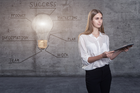 Beautiful business woman against a concrete wall with sketch drawn on it and bright lightbulbの写真素材