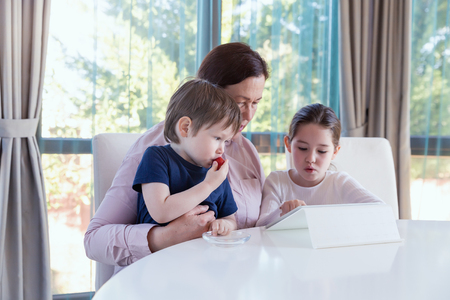 Grandma entertaining her little grandchildren with a tablet computer gameの写真素材