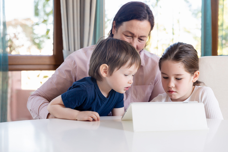 Grandma entertaining her little grandchildren with a tablet computer gameの写真素材