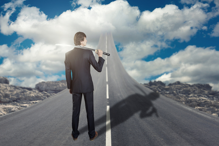 Businessman with katana sword standing on road that goes up to the skyの写真素材