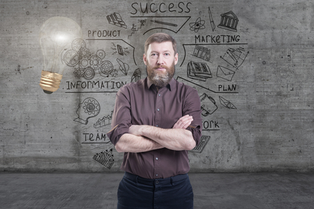 Handsome businessman against a concrete wall with sketch drawn on it and bright lightbulbの写真素材