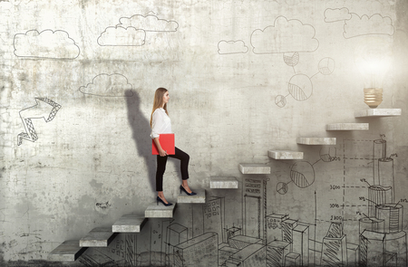Side view of young businesswoman climbing the stairs with idea lamp on concrete backgroundの写真素材
