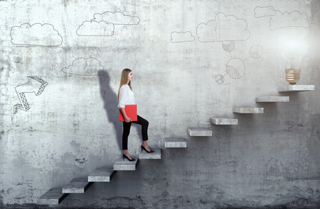 Side view of young businesswoman climbing the stairs with idea lamp on concrete backgroundの写真素材