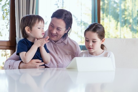 Grandma entertaining her little grandchildren with a tablet computer gameの写真素材
