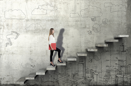 Side view of young businesswoman climbing the stairs with business sketch on concrete backgroundの写真素材