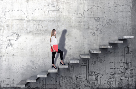Side view of young businesswoman climbing the stairs with business sketch on concrete backgroundの写真素材