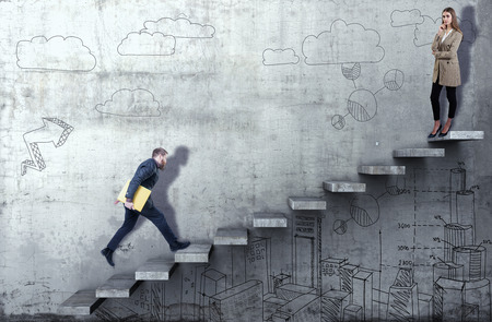 Side view of a businessman climbing the stairs with woman standing on top on a concrete backgroundの写真素材