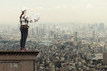 Female engineer holding construction plans standing on the roof top above a cityの写真素材