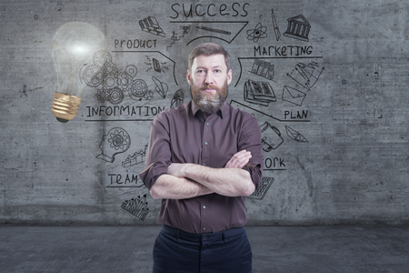 Handsome businessman against a concrete wall with sketch drawn on it and bright lightbulbの写真素材