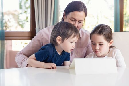 Grandma entertaining her little grandchildren with a tablet computer gameの写真素材