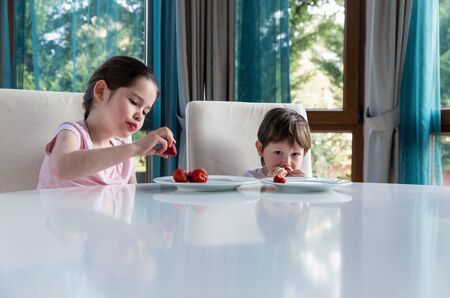 Cute children eating fresh ripe strawberries at homeの写真素材