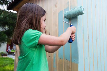 Young girl painting little wooden house with a rollerの写真素材
