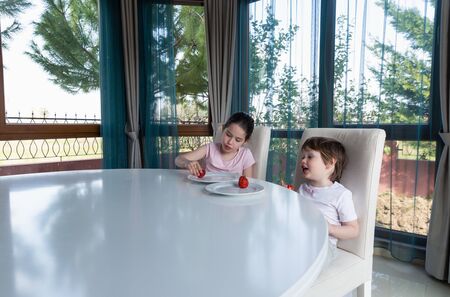 Cute children eating fresh ripe strawberries at homeの写真素材
