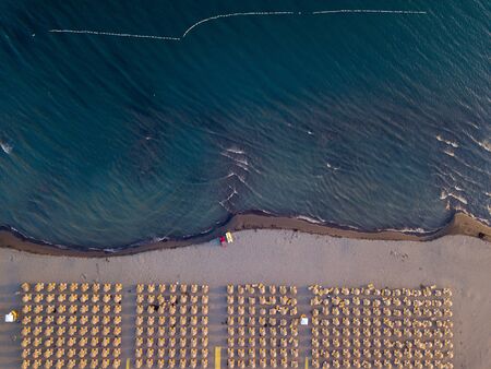 Aerial view of sandy beach with yellow sunbeds and wooden umbrellas at sunsetの写真素材