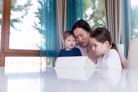 Grandma entertaining her little grandchildren with a tablet computer gameの写真素材