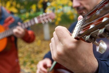 Two friends playing guitars in autumn park